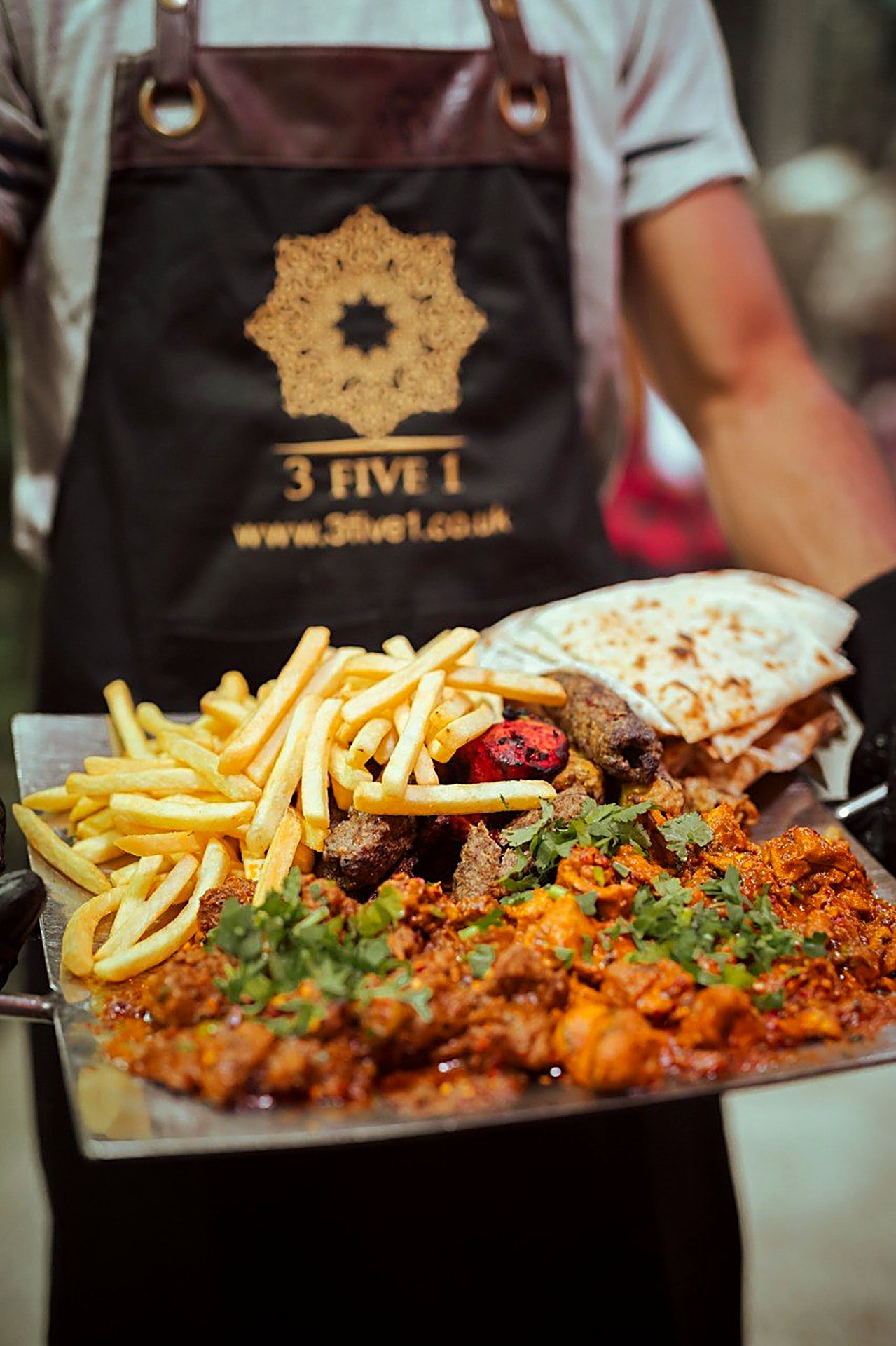 A 3 Five 1 team member bringing out a sizzling tawa platter of grills, curry, chips and naan